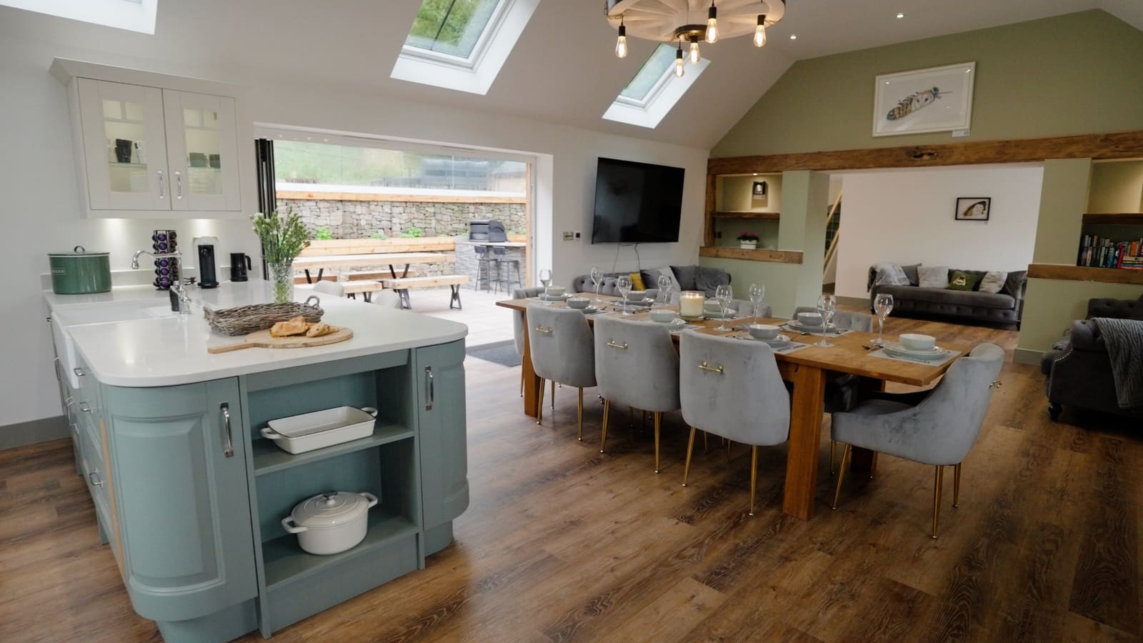 The sage-green kitchen island beside the dining table, with bifold doors open onto the courtyard.