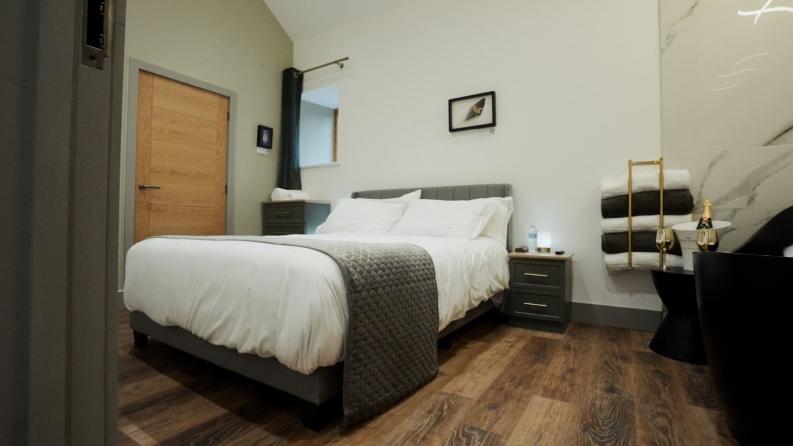 A king bedroom with white bedding, a grey throw and a freestanding black bath by a marble wall.