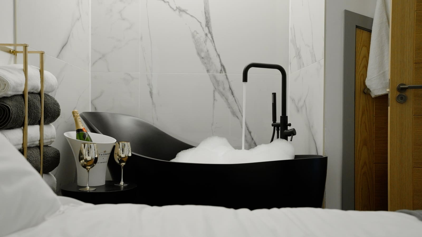 The black stone bath filling, with champagne on ice and two glasses beside it.