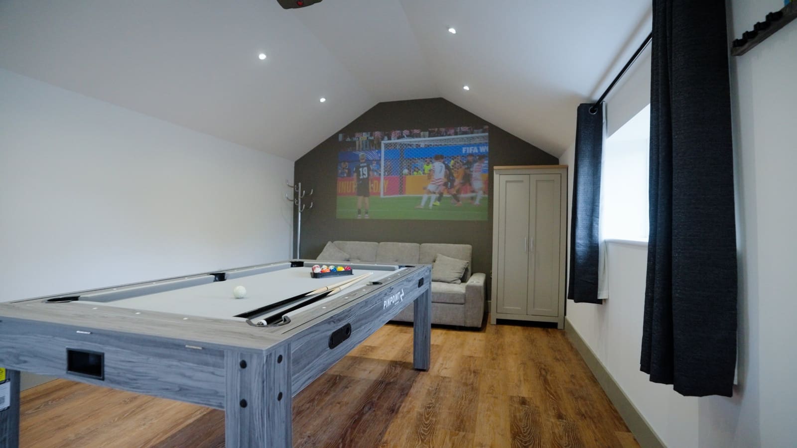 The games barn: a pool table and sofa, with a film projected on the end wall.
