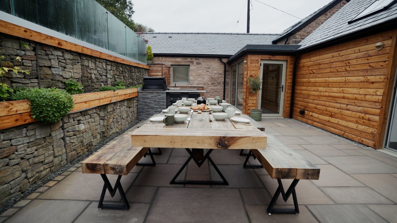 The courtyard dining table set for breakfast, beside the outdoor kitchen and timber-clad barn.