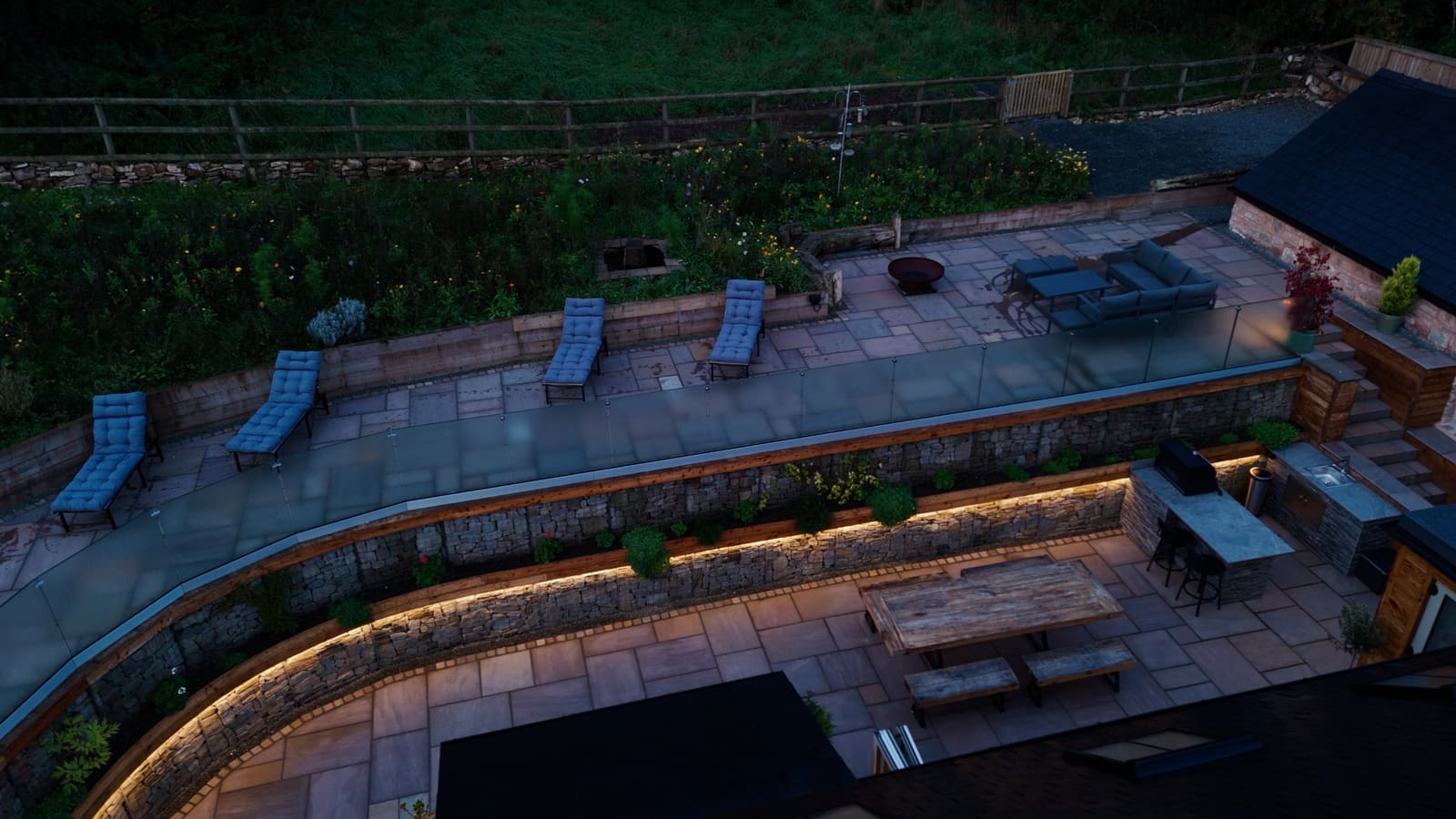 Loungers on the upper terrace above the lit courtyard, with the wildflower bank behind.