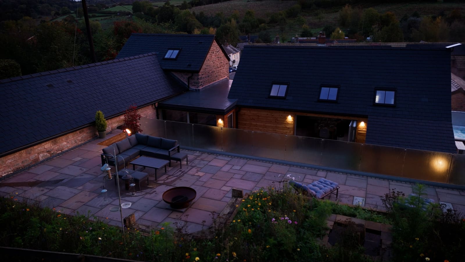 The upper terrace at dusk with outdoor sofas and a fire pit, the barn lit beyond.