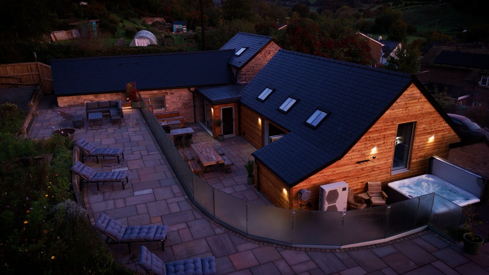 The barn and its terraces from the air at dusk, loungers curving around the glass balustrade.