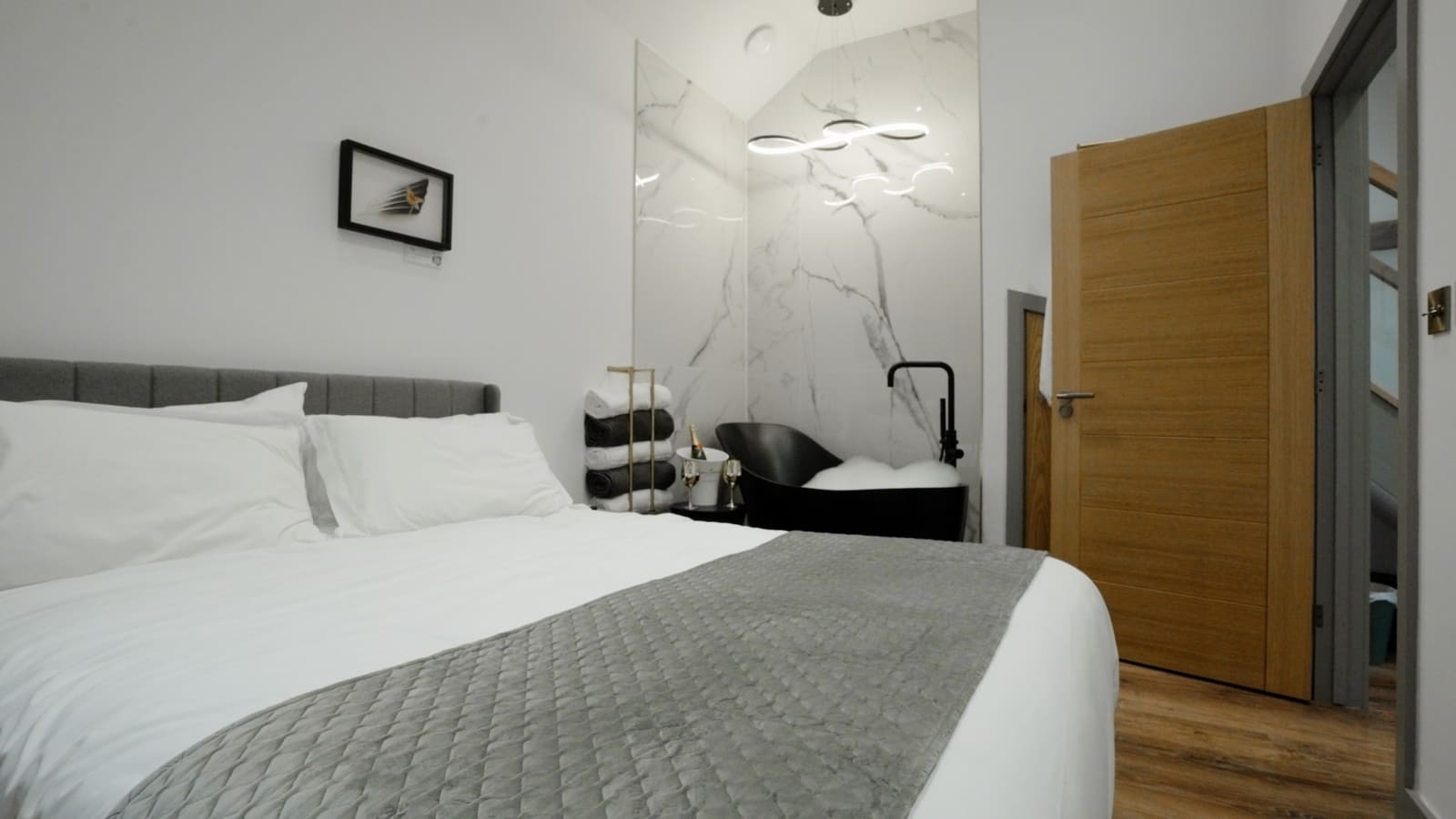 A king bedroom with crisp white bedding, a grey throw and an oak door.