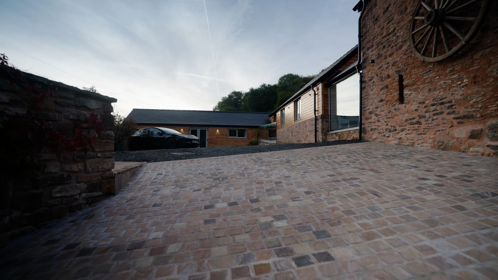 The timber bike store at dusk, with the wash-down hose reel and charger on the wall and a car charging alongside.