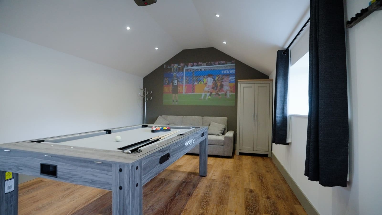 The games barn: a pool table, a sofa and a film projected on the end wall under a vaulted ceiling.