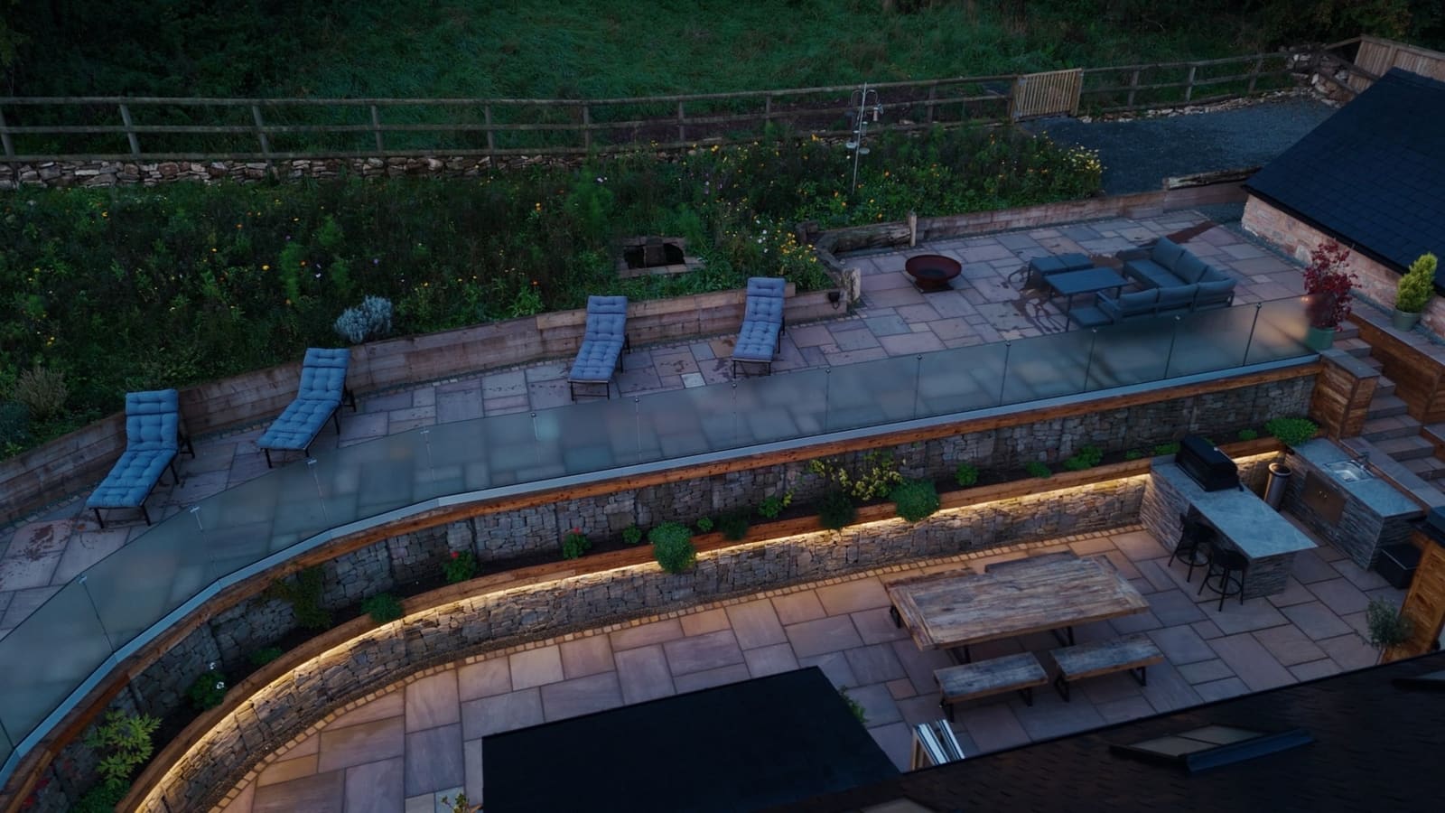 The terraces from above at dusk: loungers, lit stone walls and the outdoor dining area.